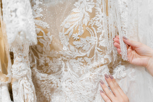 Mariée touche robe de mariée luxueuse crème blanche sur cintres. Robes en mousseline de soie, tulle et dentelle. Pendentifs perles et cristaux de luxe sur les manches d'une couleur délicate d'une robe de mariée
 - Photo, image