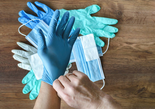 ανδρικά χέρια σε γάντια γόμα στο παρασκήνιο της προστασίας από ιατρικές μάσκες COVID-19 σε ξύλινο φόντο γκρο πλαν - Φωτογραφία, εικόνα