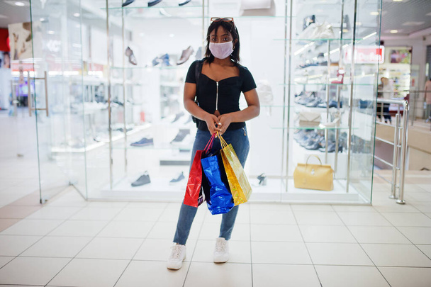 African american woman wearing face protective medical mask for protection from virus disease with shopping bags in mall during coronavirus pandemia. - Zdjęcie, obraz