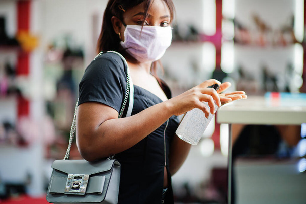 African american woman wearing face protective medical mask for protection from virus disease in shoes store use hand sanititzer during coronavirus pandemia. - Foto, afbeelding