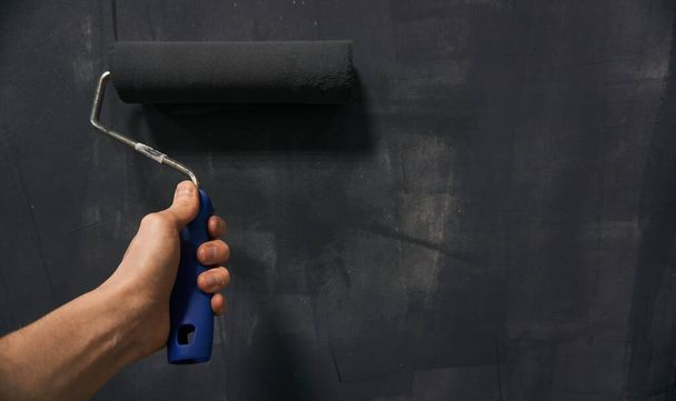 The man's hand holds a roller with black paint. Wall painting . Home repair. - Photo, Image
