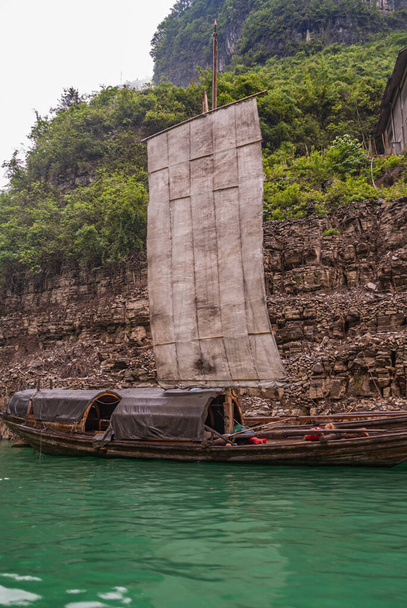Wushan, Chongqing, China - May 7, 2010: Mini Three Gorges on Daning River. Round cabins on sloops with sail docked gainst brown cliffs with higher up green vegetation and on emerald green water. - Photo, Image