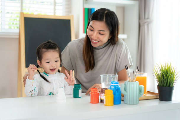 Aziatisch kleuterschool meisje met moeder schilderen gips pop met acryl aquarel verf in de woonkamer thuis. Thuisonderwijs en afstandsonderwijs - Foto, afbeelding