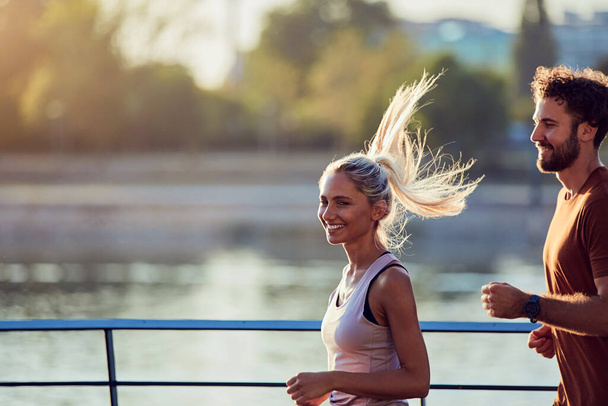 Moderne vrouw en man joggen / sporten in stedelijke omgeving bij de rivier. - Foto, afbeelding