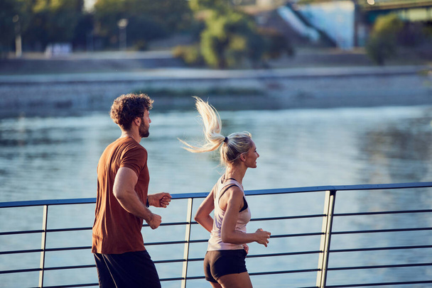 Сучасна жінка і чоловік бігають / вправляються в міському оточенні біля річки
. - Фото, зображення