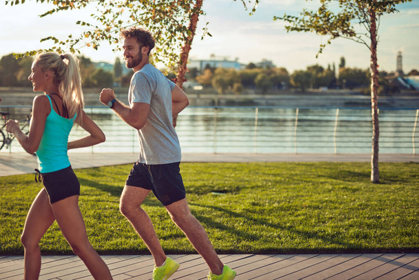 Nowoczesna kobieta i mężczyzna jogging / ćwiczenia w środowisku miejskim w pobliżu rzeki. - Zdjęcie, obraz