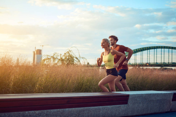 Современная женщина и мужчина бег трусцой / упражнения в городских окрестностях у реки. - Фото, изображение