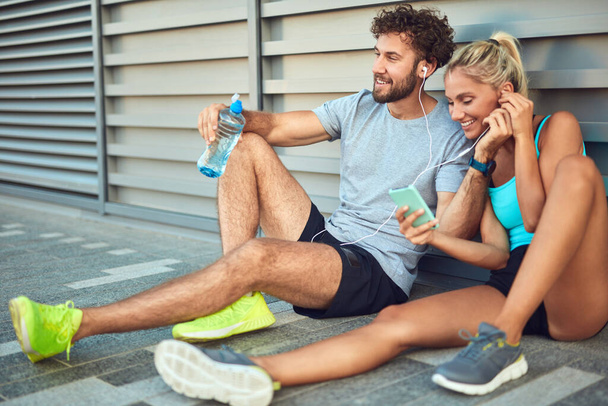 Couple moderne faisant une pause sur le trottoir pendant le jogging / exercice. - Photo, image