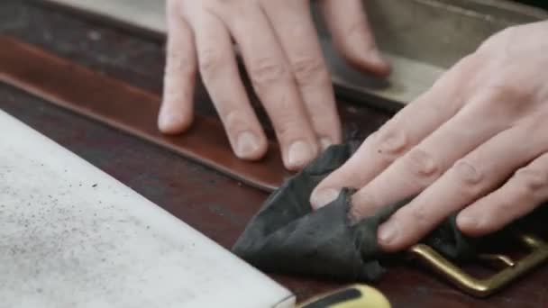 Primer plano de hombre curtidor toallitas con un paño un nuevo cinturón de cuero en el taller de cuero. Proceso de trabajo del cinturón de cuero en el taller de cuero
. - Imágenes, Vídeo