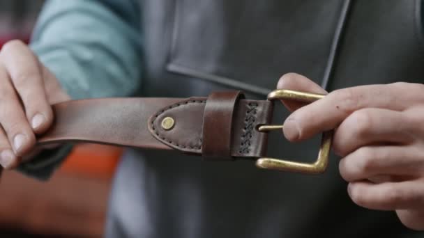 Gros plan de l'homme avec tablier vérifie une nouvelle ceinture en cuir marron dans l'atelier de cuir. Processus de travail de la ceinture en cuir dans l'atelier de cuir
. - Séquence, vidéo