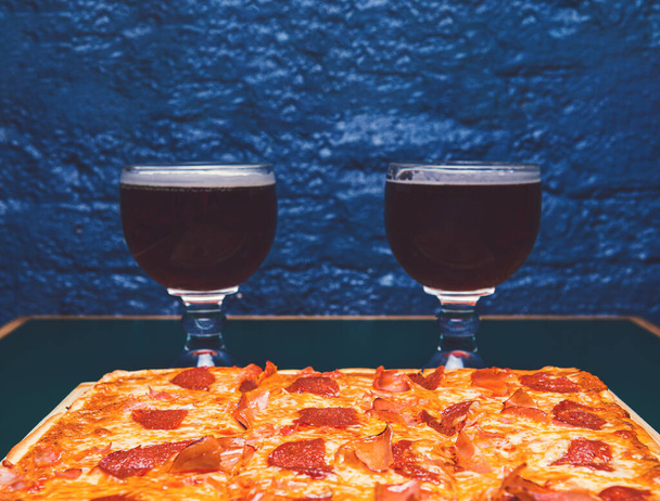 négyzet alakú pizza és sör sötét hangulatú világításban - Fotó, kép