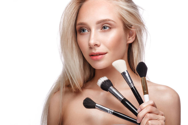 Beautiful young girl with a light natural make-up, brushes for cosmetics and nude manicure. Beauty face. - Foto, afbeelding