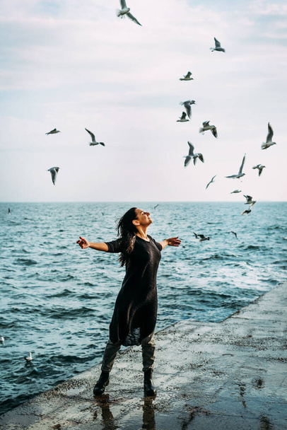 Девушка в черном стоит на пирсе с распростертыми объятиями к солнцу, и ветер получает вдохновение и силу и внутренний покой от чаек души. Открытые для вызовов и возможностей жизни
 - Фото, изображение