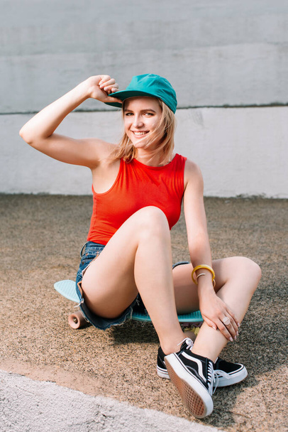 bright, athletic and sexy girl with blond hairs dressed very stylish, she is sitting on her skateboard and laughing - Foto, Imagem