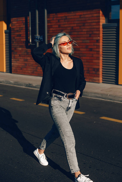 Stunning fashionable woman with blue hair and red eyeglasses posing outside in the street during a sunny day - Foto, Bild