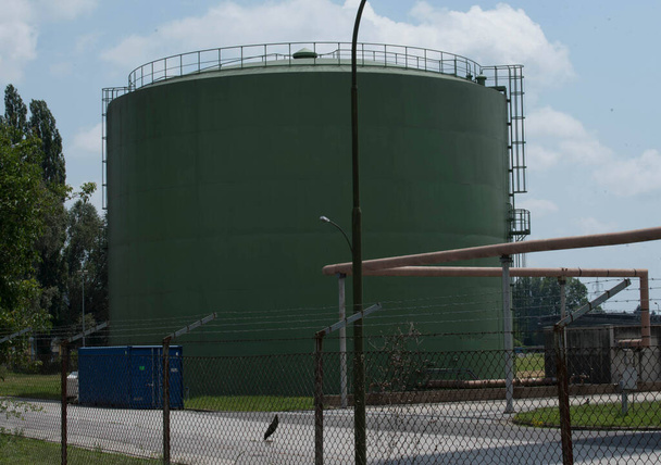 een groene olietank in een omheinde olietankboerderij - Foto, afbeelding
