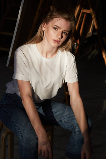 Молода дівчина в білій футболці сидить на дерев'яному стільці
 - Фото, зображення