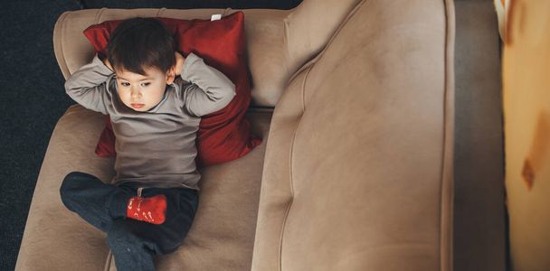 Hübscher kaukasischer Junge liegt mit gekreuzten Händen und Beinen auf dem Sofa, während er irgendwo sucht - Foto, Bild