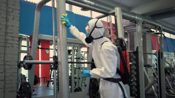 pracovník dezinfikuje tělocvičnu fitness vybavení z coronavirus covid-19 nebezpečí s antibakteriální dezinfekční postřikovač na karanténní muž v ochranném obleku čistí výcvikový přístroj na cvičišti. - Záběry, video
