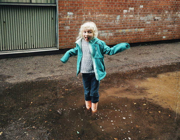 Preschool girl jumping in muddy puddle. Seasonal spring summer kids activity outdoor. Active child kid having fun outside and enjoying life. Happy childhood lifestyle. Motion action blur. - Photo, Image