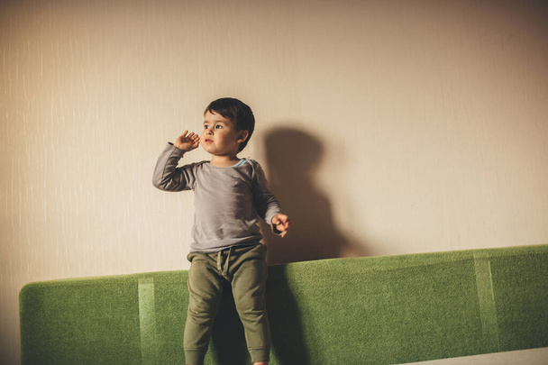 Bored caucasian boy sitting on the sofa and looking to the window enthusiastically - Photo, Image