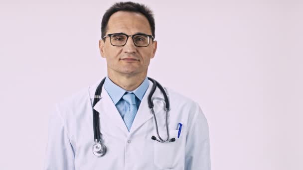 Arzt mittleren Alters mit schneeweißem Lächeln zieht Hand nach vorne und zeigt Daumen - Filmmaterial, Video