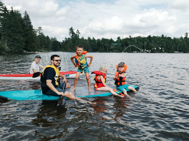 Pères avec enfants nageant sur la planche à pagaie sur le lac. Papas avec des enfants faisant du sport activité aquatique d'été en plein air. Saisonnière recreation water entertainment. Amis sportifs de la famille
.  - Photo, image