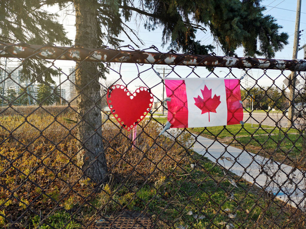 Toronto, Ontario, Kanada - 28 Nisan 2020: Kırmızı kalp ve Kanada bayrağı tel örgülü açık havada. Covid-19 salgını sırasında gerekli çalışanlara ve sağlık hemşirelerine teşekkür ederim.. - Fotoğraf, Görsel
