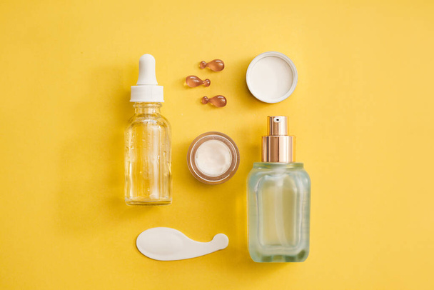 Konzept zur Hautverjüngung - Glasserumflasche, Augencreme, Gesichtsölkapseln auf gelbem Hintergrund. - Foto, Bild