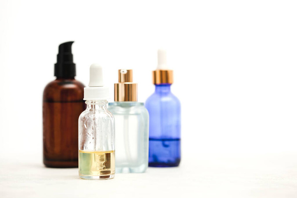 Set of colorful glass bottles with skin care products on white background with copy space. Face serums, acids and packages for essencial oils. - Фото, изображение