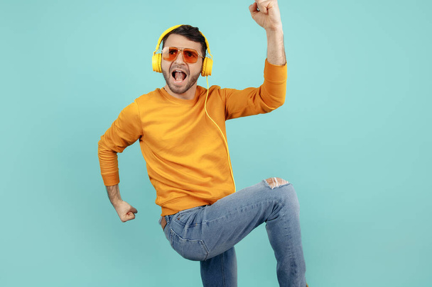 Excited bearded young man wearing sunglasses listening to music celebrate success over cyan background. - Foto, Imagem