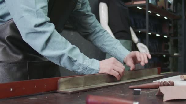 Un tanneur professionnel met de la pâte sur le bord d'une ceinture en atelier. Processus de travail de la ceinture en cuir dans l'atelier de cuir
. - Séquence, vidéo