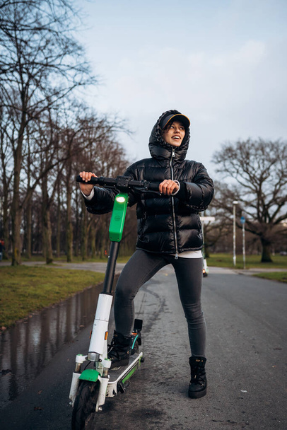 Woman in a jacket on an electric scooter in an autumn park. - Photo, Image
