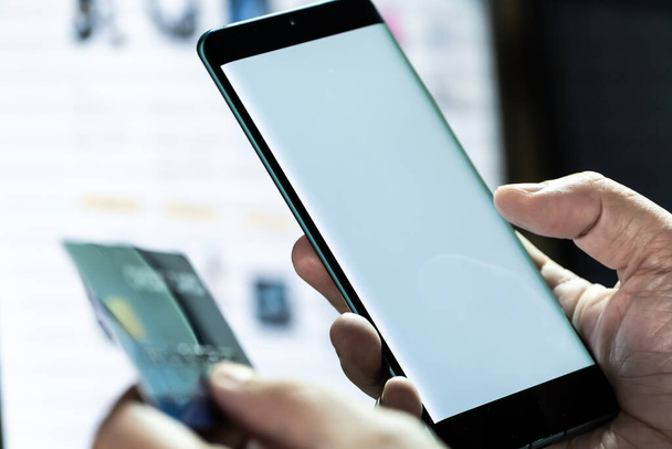 Mock up Handy und Kreditkarte in der Hand mit Monitor-Hintergrund. Konzept für mobile Anwendungstechnologie und Online-E-Commerce. - Foto, Bild