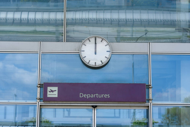 Close-up de um relógio sobre portas do aeroporto de vidro fechado com um sinal de partidas
 - Foto, Imagem