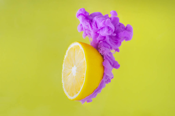 Φέτα λεμόνι με μερική εστίαση της διάλυσης βιολετί αφίσα χρώμα στο νερό σε κίτρινο φόντο για το καλοκαίρι, αφηρημένη και φόντο έννοια. - Φωτογραφία, εικόνα