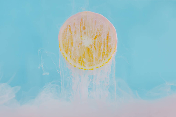 Θολή εστίαση της διάλυσης ροζ αφίσα χρώμα στο νερό με φέτα λεμόνι σε μπλε φόντο για το καλοκαίρι, αφηρημένη και φόντο έννοια. - Φωτογραφία, εικόνα