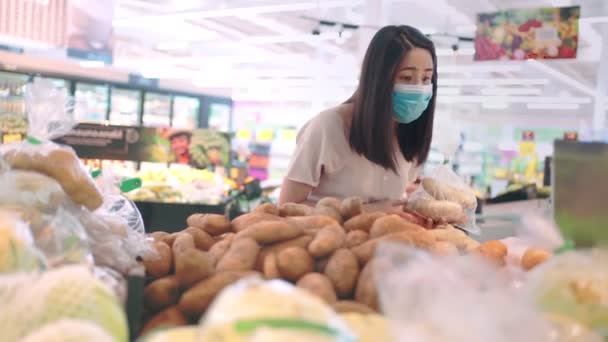 Молода азіатка жінка носить маску антикарантинної концепції, в продуктовому магазині, життя під час пандемічної кризи вірусу Конід-19, супермаркет овочевої картоплі шельф, світова економічна криза, забруднений об'єкт. - Кадри, відео