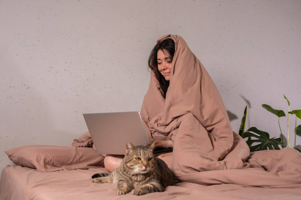 The concept of social distance and isolation. Work from home remotely over the Internet. A young woman works at home on a computer and a cat is next to her. Quarantine. Copy space. - Fotó, kép