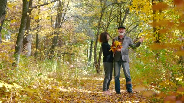 Ein fröhliches älteres Ehepaar mit Bart und einem Strauß Blätter lachte, genoss einen Spaziergang und verbrachte Zeit miteinander in einem gemütlichen Herbstwald zwischen den Bäumen. Älterer Mann rollt ab. - Filmmaterial, Video