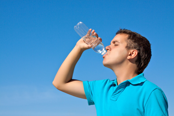 Joven macho bebiendo agua contra el cielo azul
 - Foto, Imagen