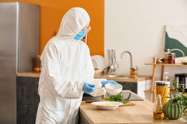 Mutfakta biyolojik tehlike kıyafeti giymiş bir kadın yemek pişiriyor. - Fotoğraf, Görsel