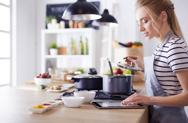 Young woman using a tablet computer to cook in her kitchen - Foto, afbeelding