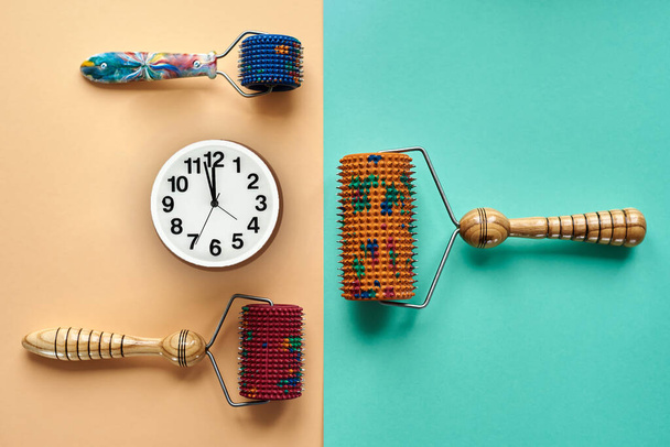 Three massager with red, orange and blue drums, metal needles lie near the clock on a yellow-green surface. top view. Thematic and promotional photography. For relaxation and health. - Photo, Image