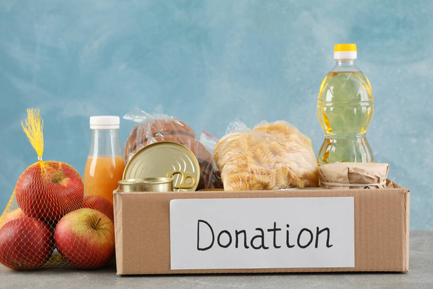 Коробка для пожертвований с разными продуктами питания на сером столе. Добровольчество
 - Фото, изображение
