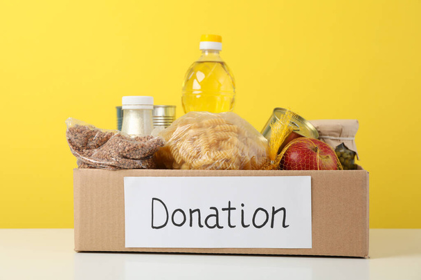 Spendenbox mit verschiedenen Lebensmitteln vor gelbem Hintergrund. Freiwilligenarbeit - Foto, Bild