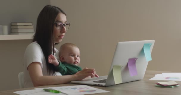 A mãe com óculos está trabalhando em um laptop. O bebé está a olhar atentamente. 4K
 - Filmagem, Vídeo