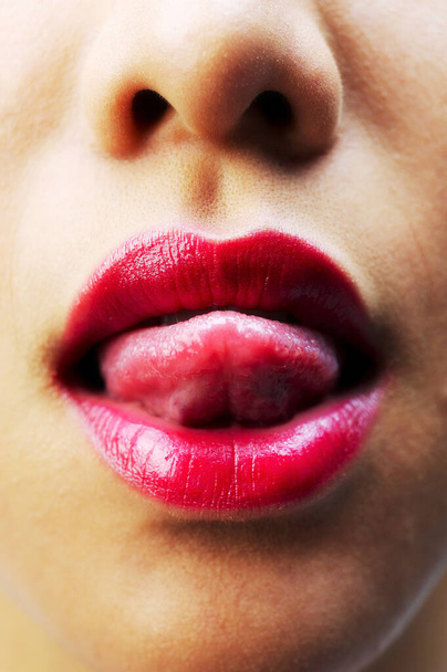 Close-up picture of woman with red lipstick sticking out her tongue - Fotó, kép