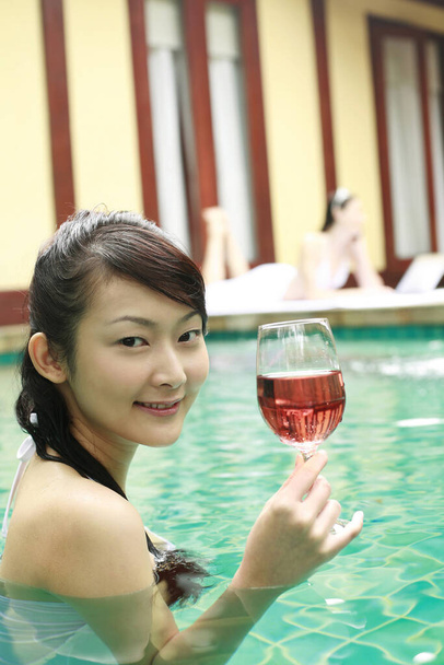 Woman enjoying a glass of red wine in the pool - 写真・画像