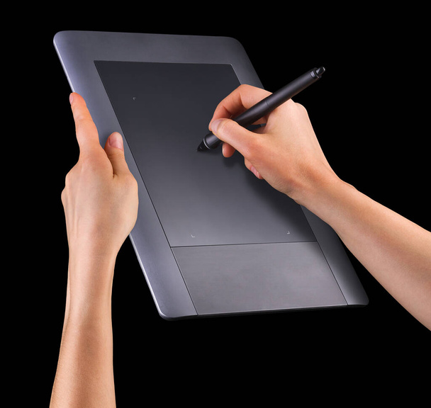 Hand holding digital graphic pen and drawing graphic tablet for illustrators, designers and photographers isolated on black background - Photo, image